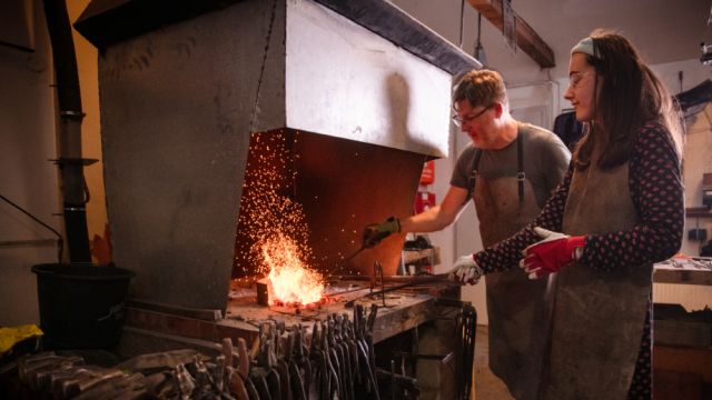 Mann und eine Junge Frau beim Schmieden vorm Ofen