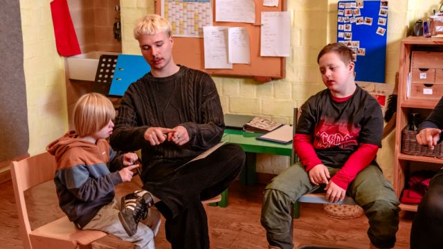 Betreuer zeigt zwei Kindern eine Fingerübung